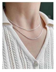 Close-up of shimmering 925 sterling silver layered chains worn on neck with white knitwear