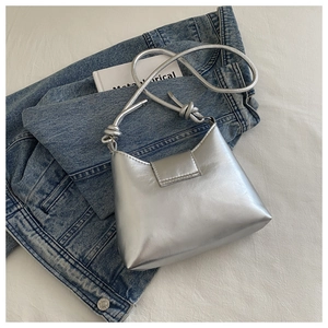 Detail of silver leather shoulder bag featuring unique woven knot strap on denim jacket