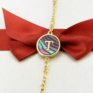 Macro detail of golden bracelet with T letter pendant and iridescent abalone shell inlay