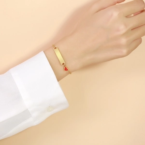 Détail d'un bracelet doré avec barre personnalisable et pendentif en forme de cœur rouge