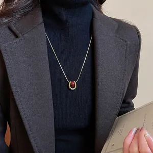 Gold-plated U-shaped pendant necklace with oval red bead on a black sweater
