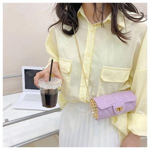 Close-up of a purple quilted cylinder chain bag worn by a model in a bright setting