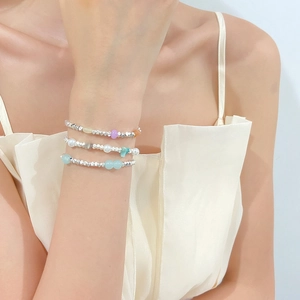 Close-up of three layered silver bead bracelets with colorful gemstones on a wrist