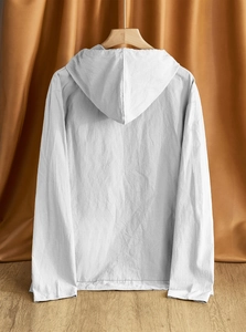 Rear view of white linen hooded shirt hanging on a wooden hanger against a fabric backdrop