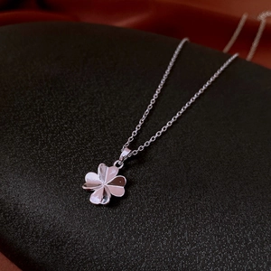 Close-up of silver four-leaf clover pendant on a cross chain over dark fabric