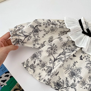 Detailed view of baby floral top with ruffle collar and black velvet bow accent