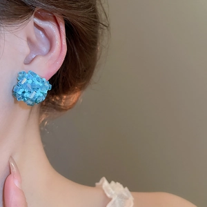 Detailansicht eines blauen Kristall-Ohrsteckers im Blumendesign, am Model präsentiert