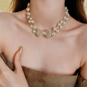 Close-up of double-layer faux pearl necklace with crystal-studded gold bow pendant
