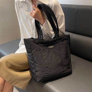 Black quilted nylon tote bag with EARE logo shown in a lifestyle shoulder carry pose
