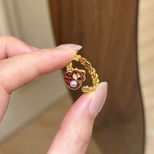 Makroaufnahme von vergoldetem Ring mit rotem Herz, Ginkgoblatt und echter Perle