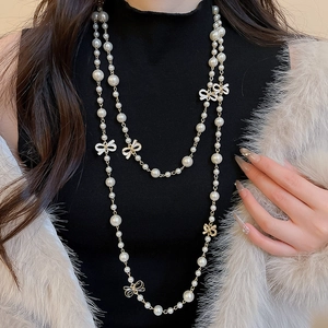 Close-up of a long pearl necklace featuring white bow charms on a black high-neck top