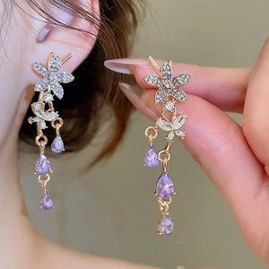 Detailed close-up of golden flower earrings with purple teardrop gems and silver butterflies