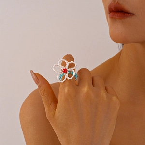 Close-up of handmade beaded flower ring with white petals and a red center on a finger