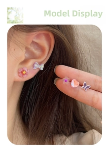 Close-up of mini floral and butterfly stud earrings with iridescent finish on ear