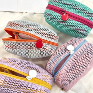 Detail showing colorful mesh mini makeup bags with large circular zippers on white fabric