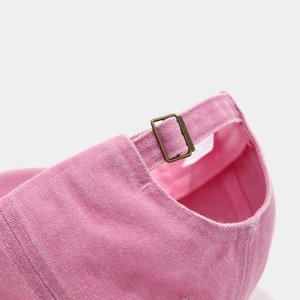 Detail of pink baseball cap featuring adjustable bronze metal buckle and washed fabric texture