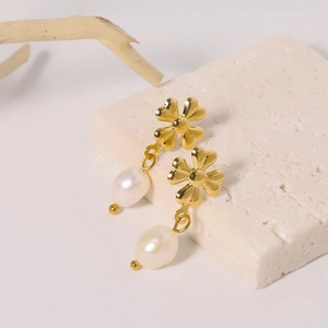 Detail of clover metal earrings with white pearl pendants on beige stone surface
