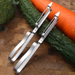 Set of two stainless steel vegetable peelers on a wooden board with fresh vegetables