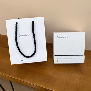 Detailed view of white minimalist jewelry gift bag and matching box on a wooden surface