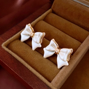 Close-up of elegant cream and gold bow earrings displayed in a brown velvet jewelry box