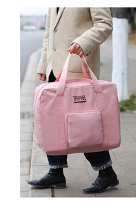 Pink waterproof nylon travel bag with Travel text held by model in outdoor setting