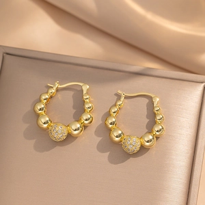 Golden titanium steel beaded hoop earrings with zircon studded ball on satin background