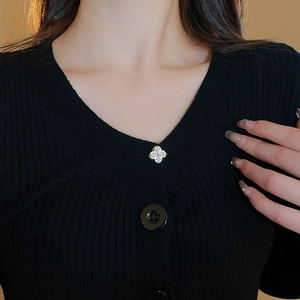 Macro detail of a sparkling silver clover brooch with crystals on a black knit sweater