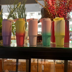 Row of colorful gradient 30oz travel mugs with carry lids on a bright display shelf