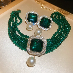 Detail of luxury emerald pendant and multilayer pearl necklace on a golden tray