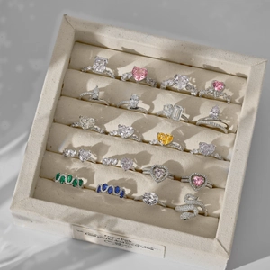 Collection of colorful zircon rings in heart and pear shapes inside a beige jewelry box