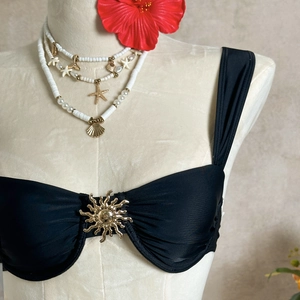 Détail du haut de bikini bandeau noir avec boucle soleil dorée et tissu en nylon brillant