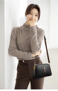 Detail of a textured black crossbody bag with gold hardware and brown strap worn by model