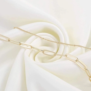 Close-up of a layered gold paperclip chain and bead bracelet on white silk fabric