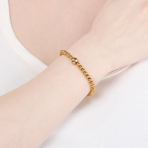Detail of 18K gold-plated beaded bracelet featuring polished steel spheres on wrist