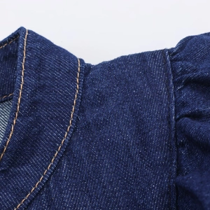 Détail macro du col de chemise en jean bleu foncé montrant la texture et l'épaule plissée