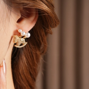 Gros plan sur boucle d'oreille cheval à bascule doré avec perle sur mannequin femme