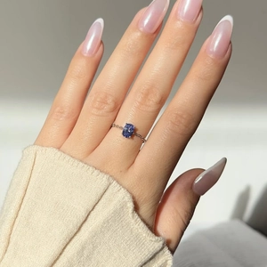 Detail of an oval dark blue zircon set on a fine silver chain ring worn on a finger
