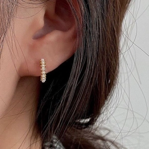 Boucles d'oreilles huggies dorées avec petites perles blanches sur le lobe