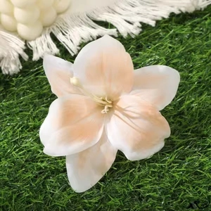 Close-up of a white lily hair clip with pink gradient petals on a green lawn