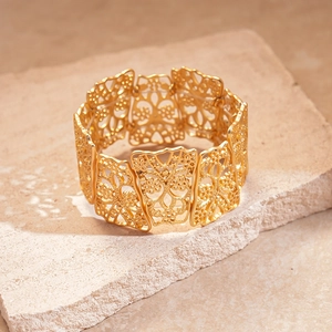 Macro detail of golden matte wide cuff bracelet with geometric floral cutout patterns
