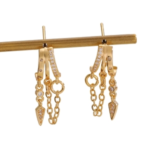 Detail of gold fringe earrings with zircon inlay and hanging chain charms on a stand