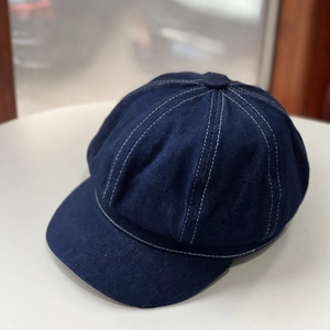 Classic dark blue denim newsboy cap with white contrast stitching on a minimalist surface