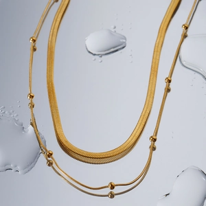 Double-layered gold bead chain and herringbone necklace with water droplet reflection