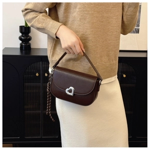 Detail of a dark brown saddle bag featuring a silver heart-shaped lock and woven strap