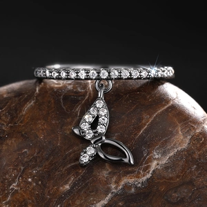 Macro detail of black plated ring with zircons and a delicate butterfly pendant charm
