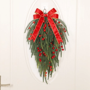 Christmas teardrop swag with pine needles, red berries and a large festive bow on white door