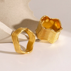 Detailed view of two gold chunky wave rings on an elegant beige textured background