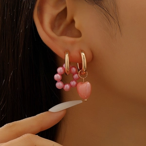 Detail of pink heart and pearl bead charms on gold hoops worn as asymmetric earrings