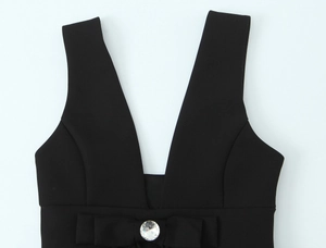 Detail eines schwarzen Midi-Kleides mit tiefem V-Ausschnitt und Kristall-Schleife