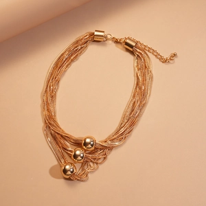 Detail of gold multi-layer chain necklace featuring metallic ball pendants and lobster clasp
